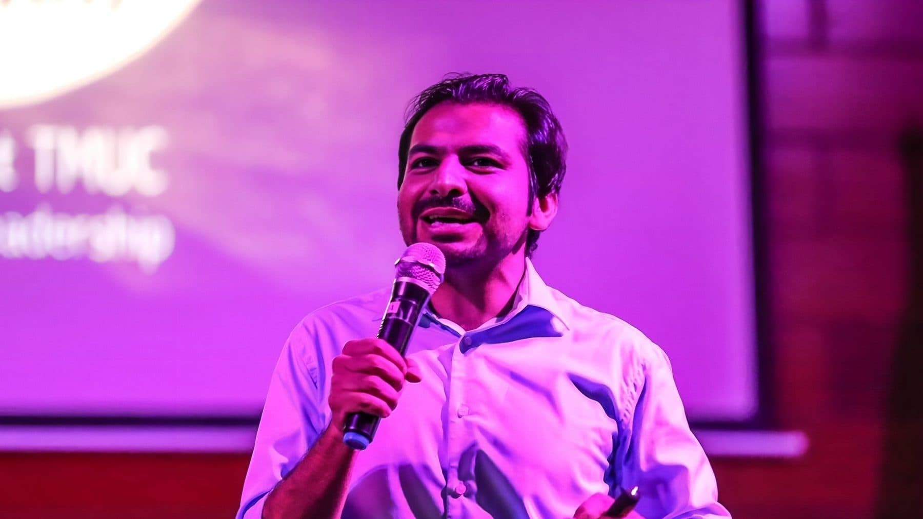 A Torque speaker on stage with a handheld mic, lit in stage colour