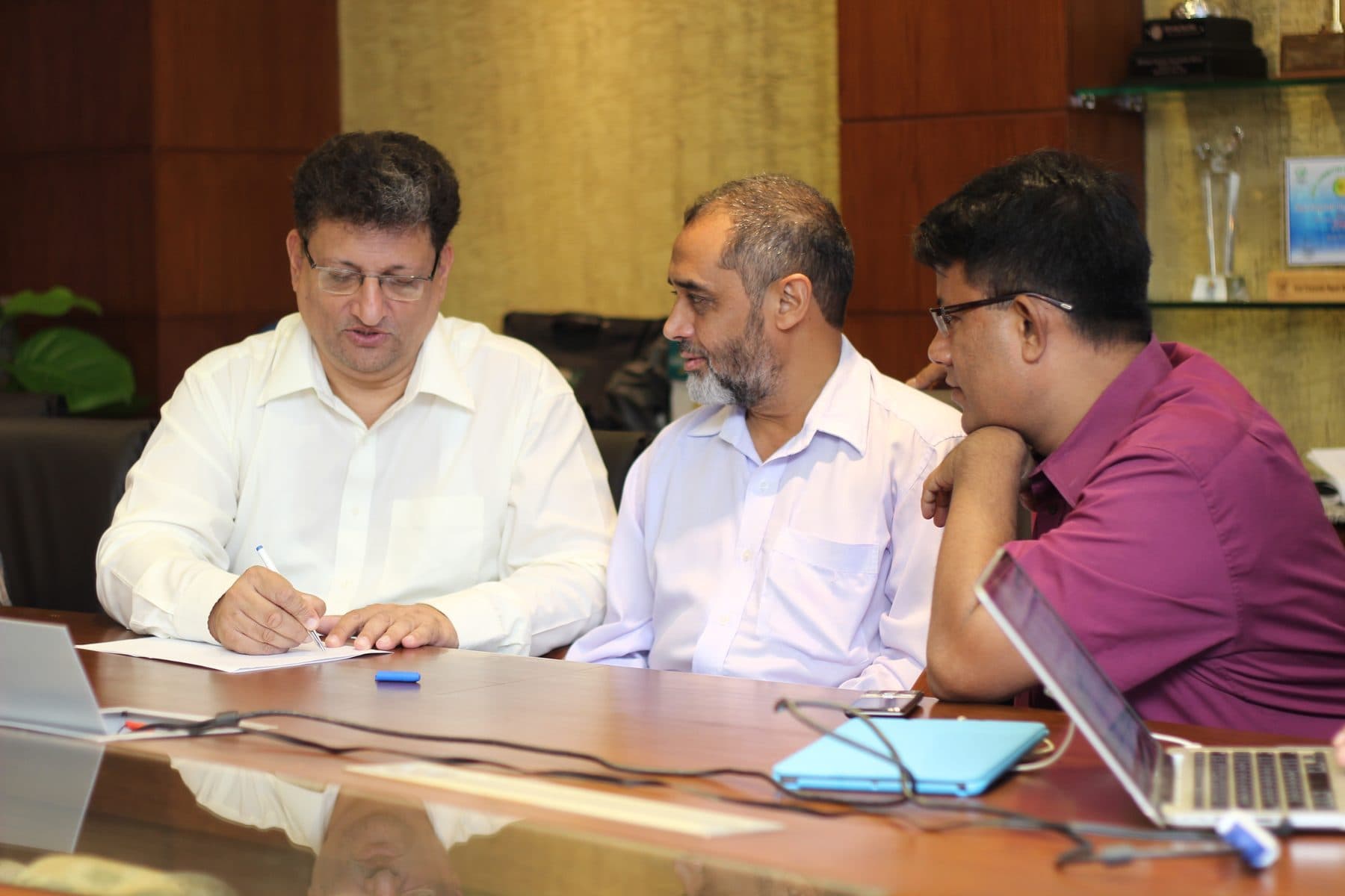 Three people working through documents and laptops around a boardroom table