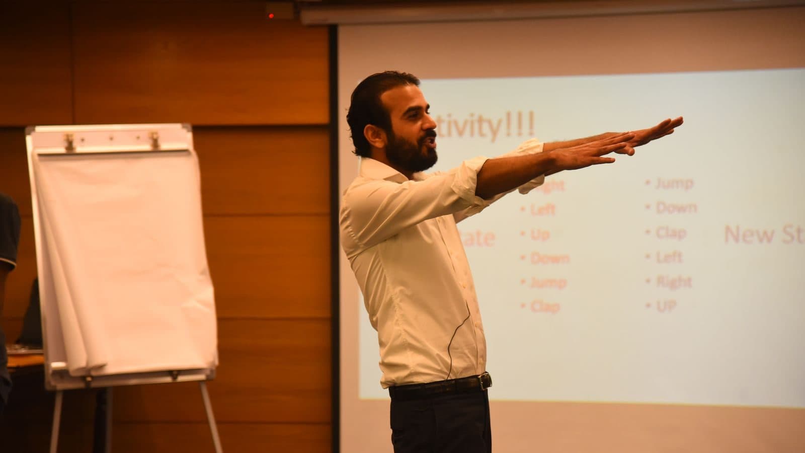 A facilitator with an arm thrown out beside a flipchart headed “Activity”, mid-instruction