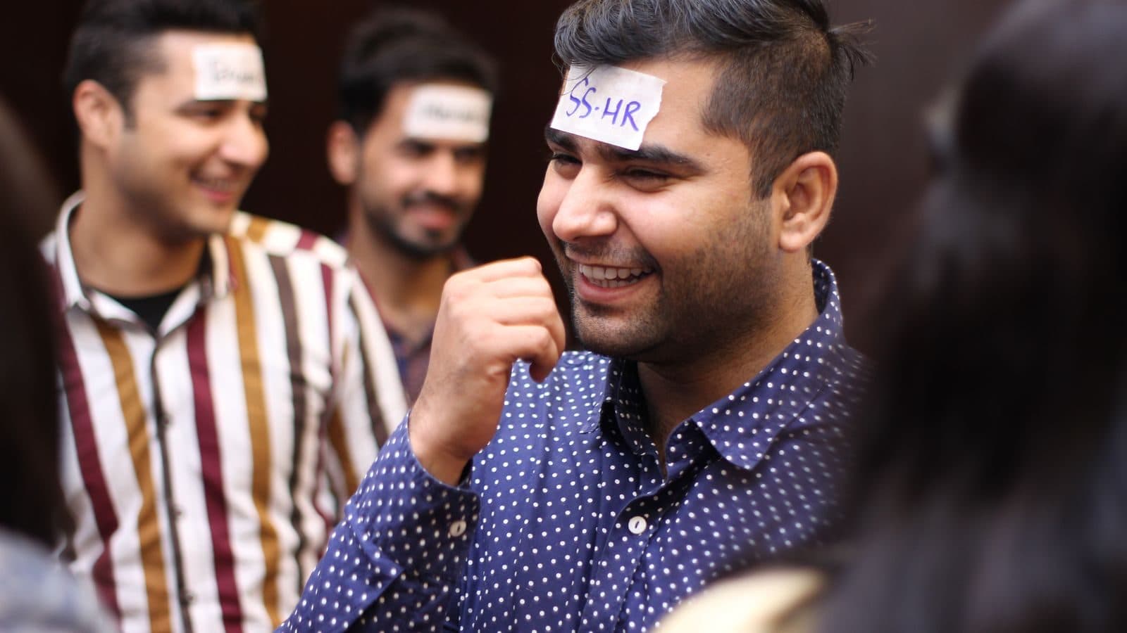 Three participants laughing, name cards stuck to their foreheads mid-exercise