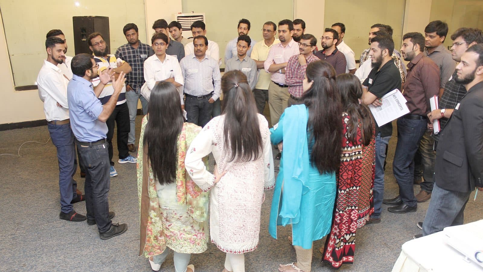 A room full of participants on their feet in small standing groups, papers in hand