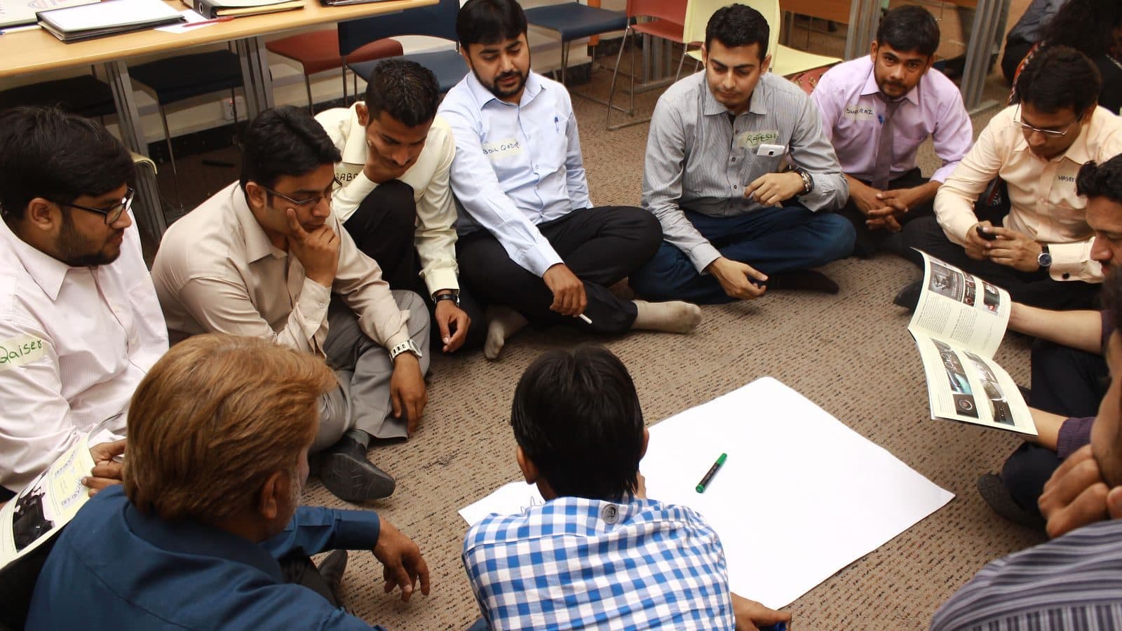 Participants sitting on the floor in a ring around a sheet of paper they are all working on