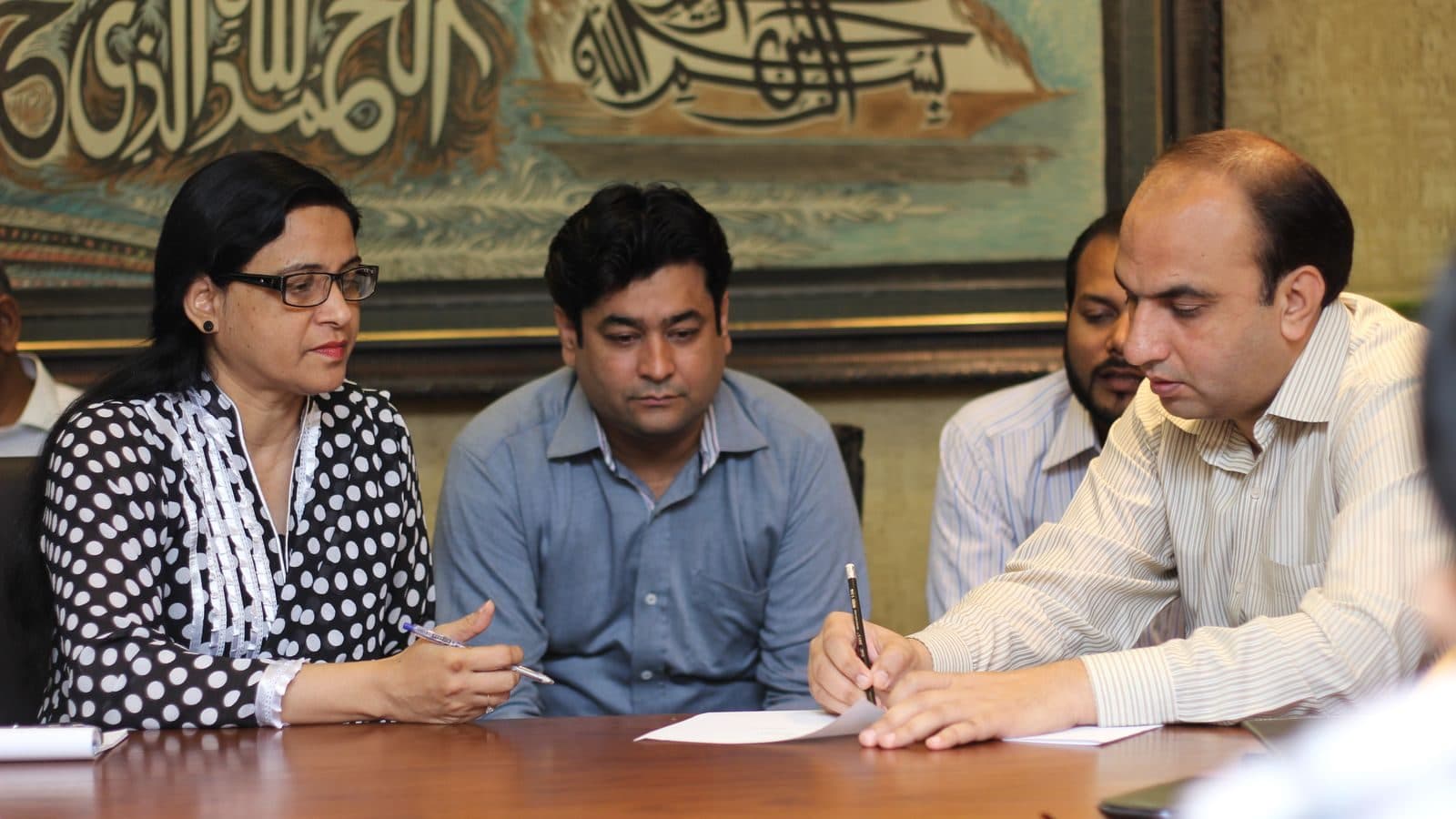 Three participants on one side of a table, one of them writing while the other two watch