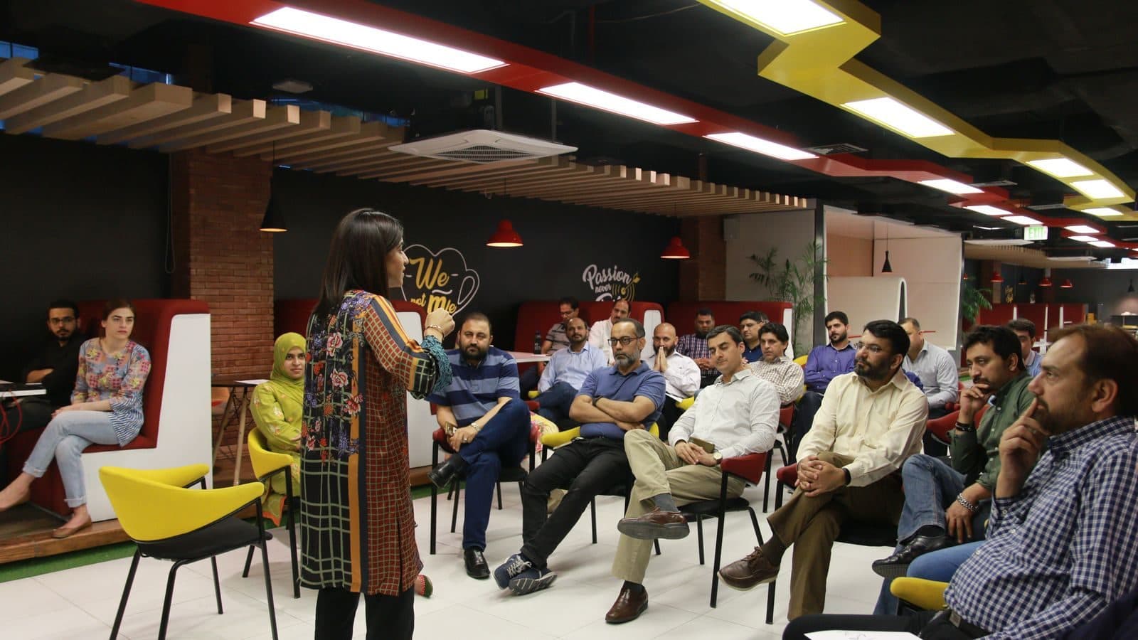 A facilitator standing to address a circle of participants in a bright open room